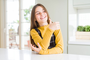 Young beautiful blonde kid girl wearing casual yellow sweater at home Looking proud, smiling doing thumbs up gesture to the side