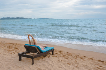 Summer beach vacation concept, Happy young Asian woman with hat relaxing on beach chair and raised arms up.