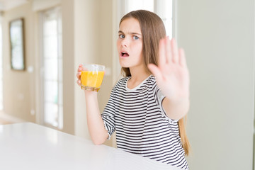Beautiful young girl kid drinking a glass of fresh orange juice with open hand doing stop sign with...