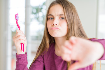 Beautiful young girl kid holding pink dental toothbrush with angry face, negative sign showing dislike with thumbs down, rejection concept