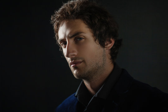 Handsome young brunette man with light eyes in dark clothes looks into the distance.