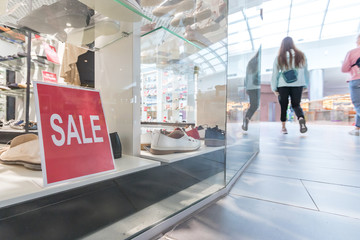 Sale sign in the shoe store shop window. Shoppers walk around the mall. Season sale, fashion and shopping concept