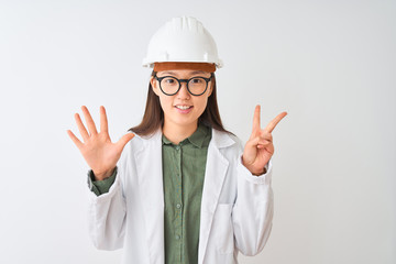 Young chinese engineer woman wearing coat helmet glasses over isolated white background showing and pointing up with fingers number seven while smiling confident and happy.