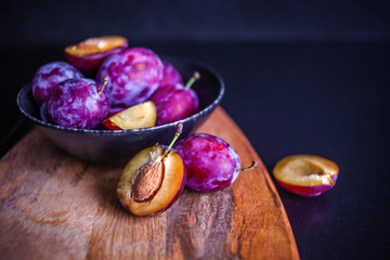 Delicious juicy blue plums in a plate on the table, textured wooden table,