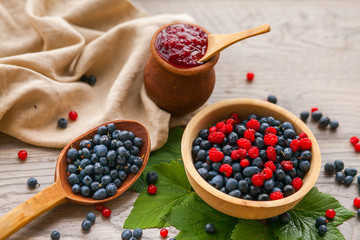 Blueberry and raspberry berry jam in a clay pot, a wooden spoon with fresh berries and a linen serviette on a wooden background