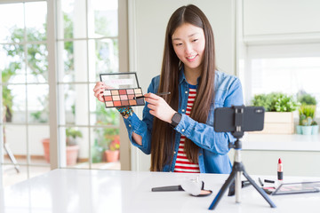 Beautiful Asian influencer woman recording make up tutorial using smartphone camera with a happy...