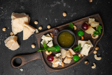 Assortment of cheese with honey, nuts and grape on a cutting board, top view.