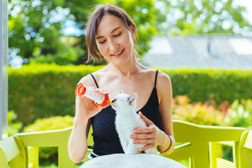 Young smiling woman feeding with milk a white cute kitten from a bottle - growing, love, care,...