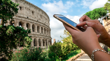 Woman messaging on the smartphone with the Coliseum of Rome at background.