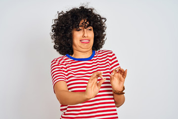 Fototapeta premium Young arab woman with curly hair wearing striped t-shirt over isolated white background disgusted expression, displeased and fearful doing disgust face because aversion reaction. With hands raised. 
