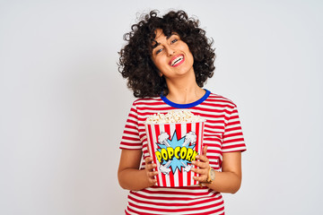 Young arab woman with curly hair holding pack of popcorns over isolated white background with a happy face standing and smiling with a confident smile showing teeth