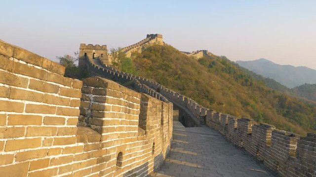 Stunning view of the ancient stone wall in China illuminated by golden evening sun. Beautiful fall colored forests cover the mountains surrounding the majestic Great Wall of China. Tourist destination