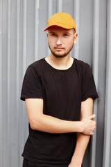 Handsome guy in a yellow cap and black t-shirt near a metal wall