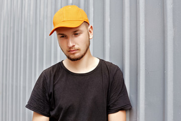 Handsome guy in a yellow cap and black t-shirt near a metal wall