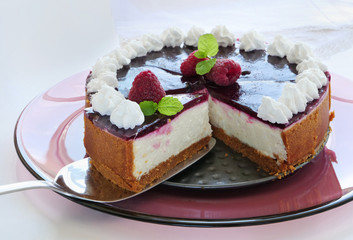 Easy no-bake cheesecake with graham cracker crust, cream cheese filling and raspberry jelly, decorated with whipped cream on white plate.