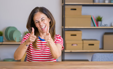 Middle age senior woman sitting at the table at home pointing fingers to camera with happy and funny face. Good energy and vibes.