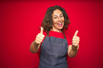 Middle age senior woman wearing apron uniform over red isolated background approving doing positive...