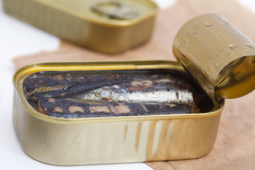 An opened can of sardines or herring in olive oil on brown paper. Sea food full of omega 3 fat.