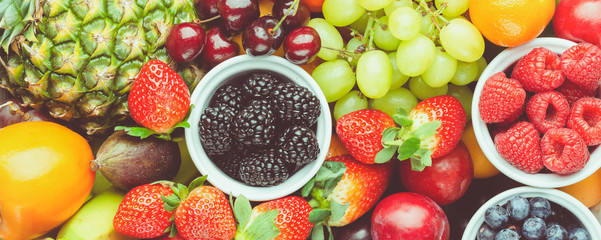 Healthy fruit background filled with strawberries raspberries oranges plums apples kiwis grapes blueberries mango persimmon pineapple, selective focus. Long photo banner, toned