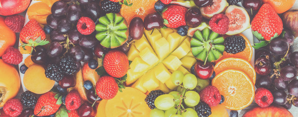Healthy fruit platter background, strawberries raspberries oranges plums apples kiwis grapes blueberries mango persimmon, top view, selective focus. Long photo banner, toned