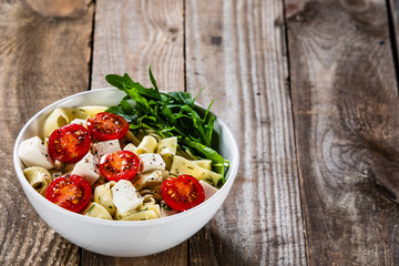 Pasta with tomatoes and white cheese on wooden table