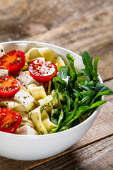 Pasta with tomatoes and white cheese on wooden table