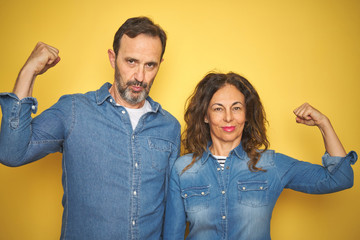 Beautiful middle age couple together standing over isolated yellow background Strong person showing arm muscle, confident and proud of power