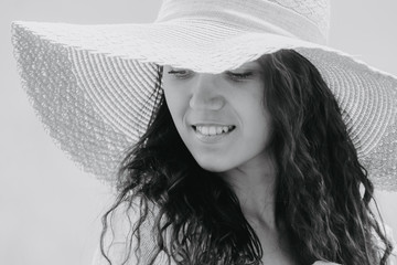 Black-white portrait of a beautiful Russian young woman close-up in a straw hat and long curly hair, a woman smiles while hiding behind a hat