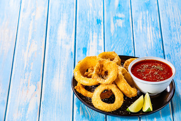 Onion rings with sauce on wooden table