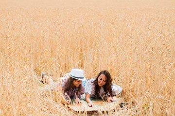 Two girls are lying in a field with a map in summer laughing.