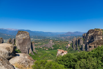 Meteora, Kalmbaka, Greece view overlooking world heritage Greek Orthodox monasteries in a green valley with village and mountains in the background. Breathtaking fairytale valley landscape.
