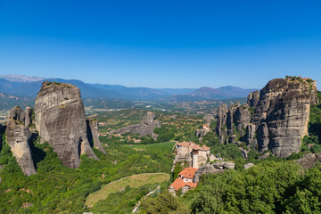 Fototapeta na wymiar Meteora, Kalmbaka, Greece view overlooking world heritage Greek Orthodox monasteries in a green valley with village and mountains in the background. Breathtaking fairytale valley landscape.