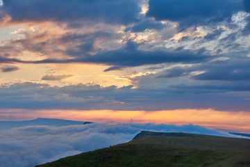 Fototapeta na wymiar Sunset clouds, blue sky and fog over a mountain green valley with a village and a winding road