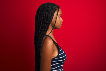 Naklejka premium Young african american woman wearing striped t-shirt standing over isolated red background looking to side, relax profile pose with natural face with confident smile.