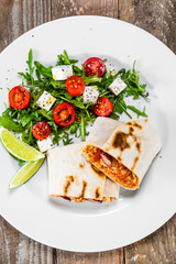 Burrito with vegetable salad on white plate