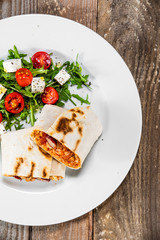 Burrito with vegetable salad on white plate
