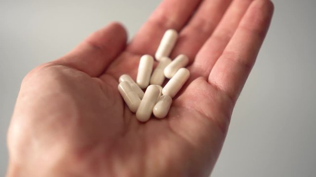 Medical white capsules fall into the palm of your hand and some fly by. on a gray background