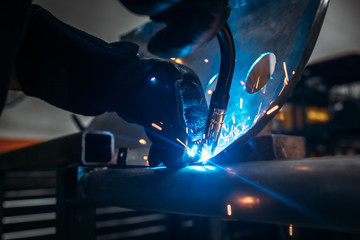Industrial Worker with protective gloves  welding motorcycle or car metal steel part at the factory workshop with a lot of sparks