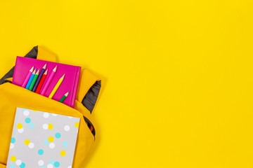 Back to school concept. Yellow backpack with school supplies on yellow background. Top view