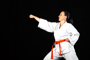 A young brunette woman in a white kimono is engaged in karate on a black background.