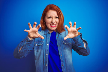 Young beautiful redhead woman wearing denim shirt standing over blue isolated background smiling...