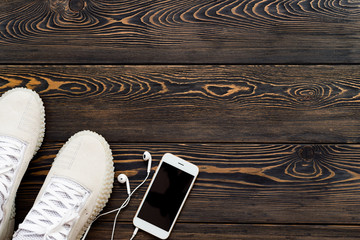 Sneakers on a dark old wooden background with a mobile phone and headphones. Place for your text.