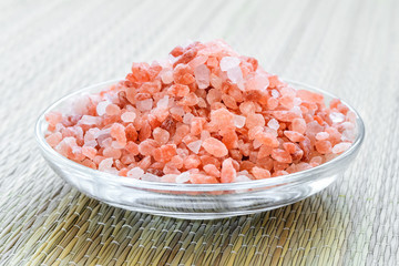 Fototapeta na wymiar Heap of pink himalayan salt crystals in a glass saucer on a rough green mat. Himalayan salt is used in cooking, medicine and cosmetology.