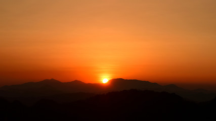 sun setting behind a dense forest area followed by mountains.	