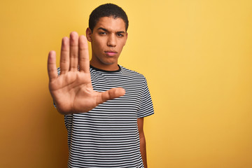 Young handsome arab man wearing navy striped t-shirt over isolated yellow background doing stop...