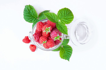 Raspberries in a jar surrounded by green leaves on a white background