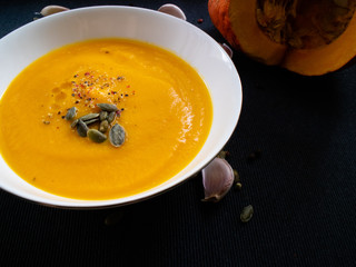 Vegetable soup with half pumpkin and some garlic cloves on a dark background