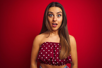 Young beautiful woman wearing casual t-shirt standing over isolated red background afraid and shocked with surprise expression, fear and excited face.