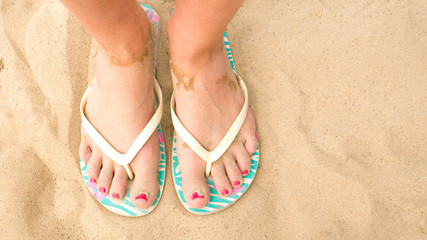 Close up of female feet wearing flip flops on sandy beach 