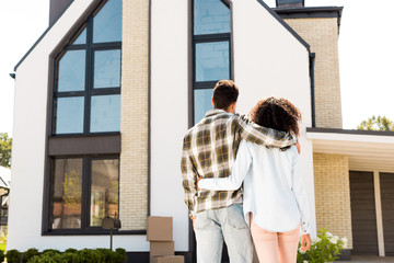 back view of african american couple hugging while looking at new house